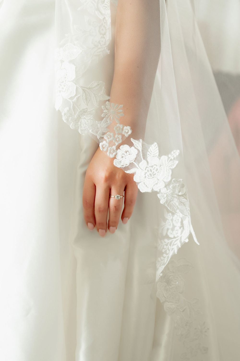 Close-up of lace details and wedding ring against white wedding dress fabric.