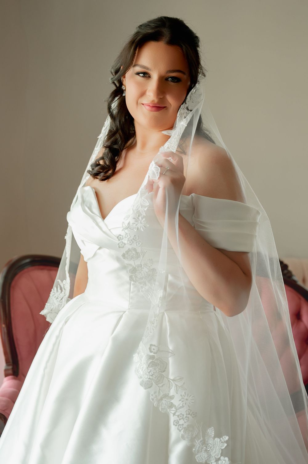 A flowing white wedding dress with delicate lace details and veil captured in an elegant indoor portrait series.