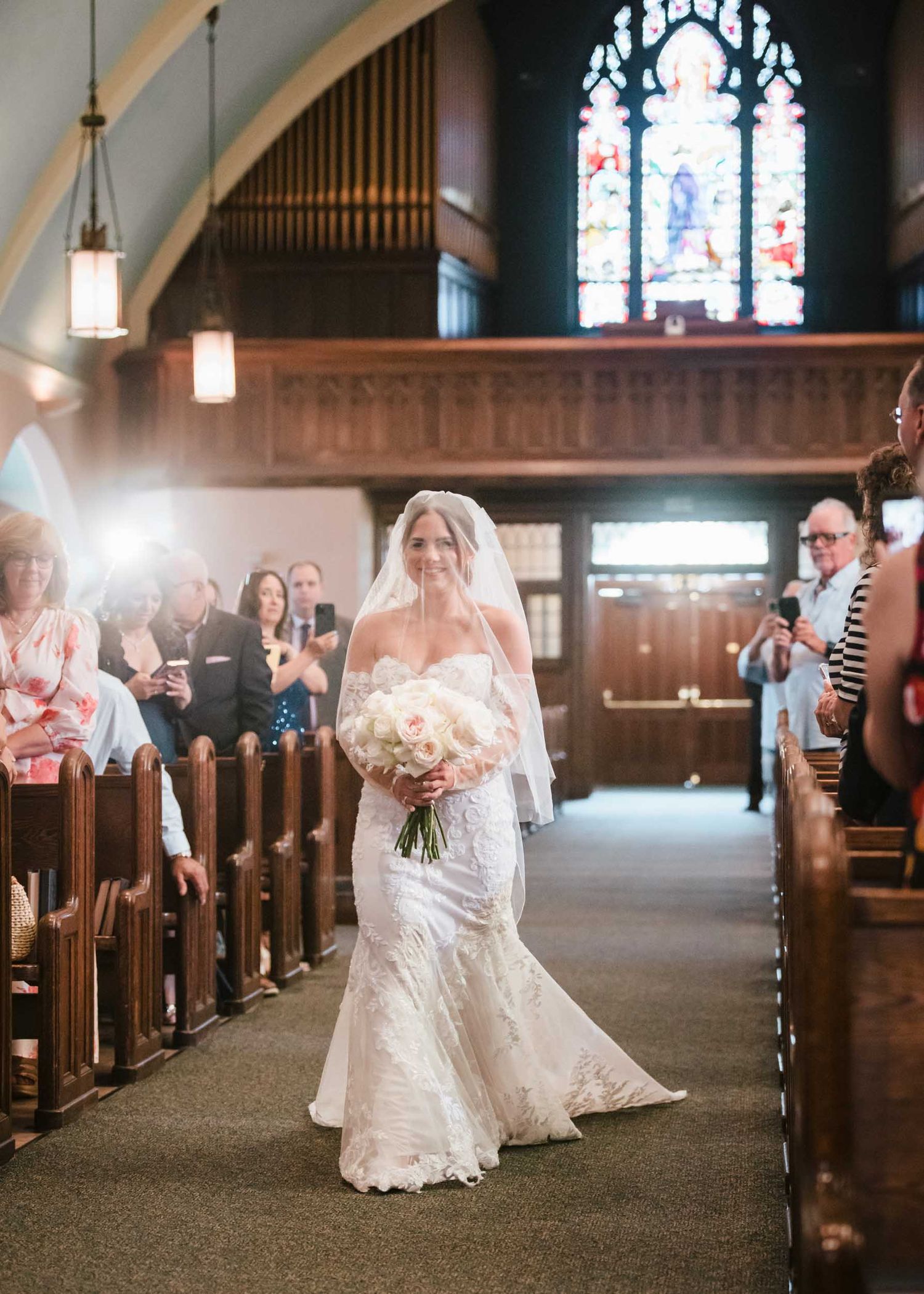 The bride walking down the aisle holding a bouquet during a wedding ceremony at Saint Brigid Church in South Boston