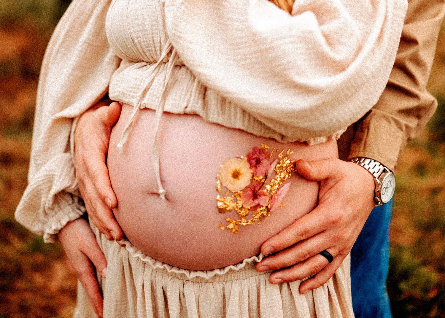 A series of maternity photos showing a pregnant belly decorated with delicate floral designs against an autumn backdrop.