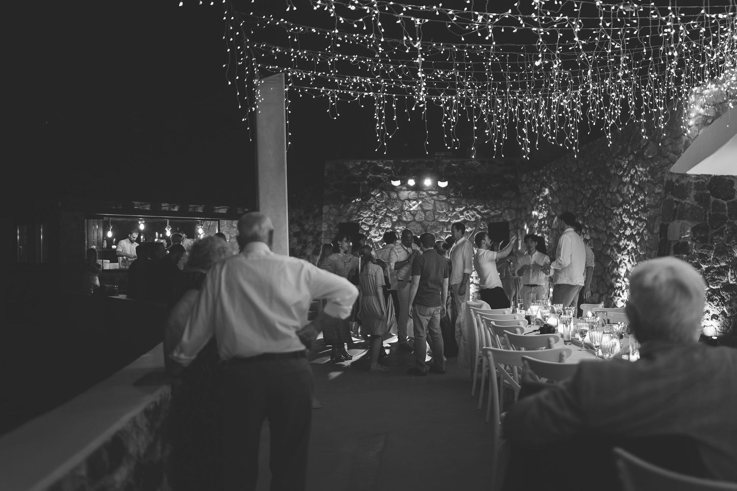 People gather at an outdoor Santorini evening wedding reception under twinkling string lights at El Viento.