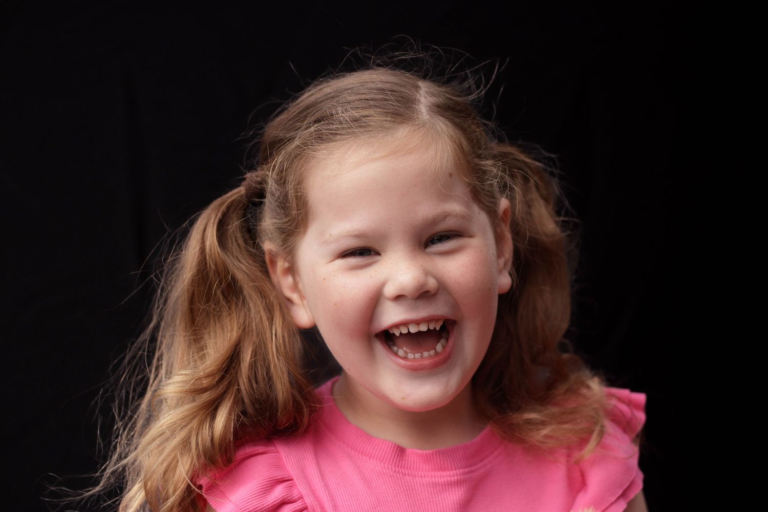 Happy young girl with pigtails laughing joyfully in a pink ruffled shirt.