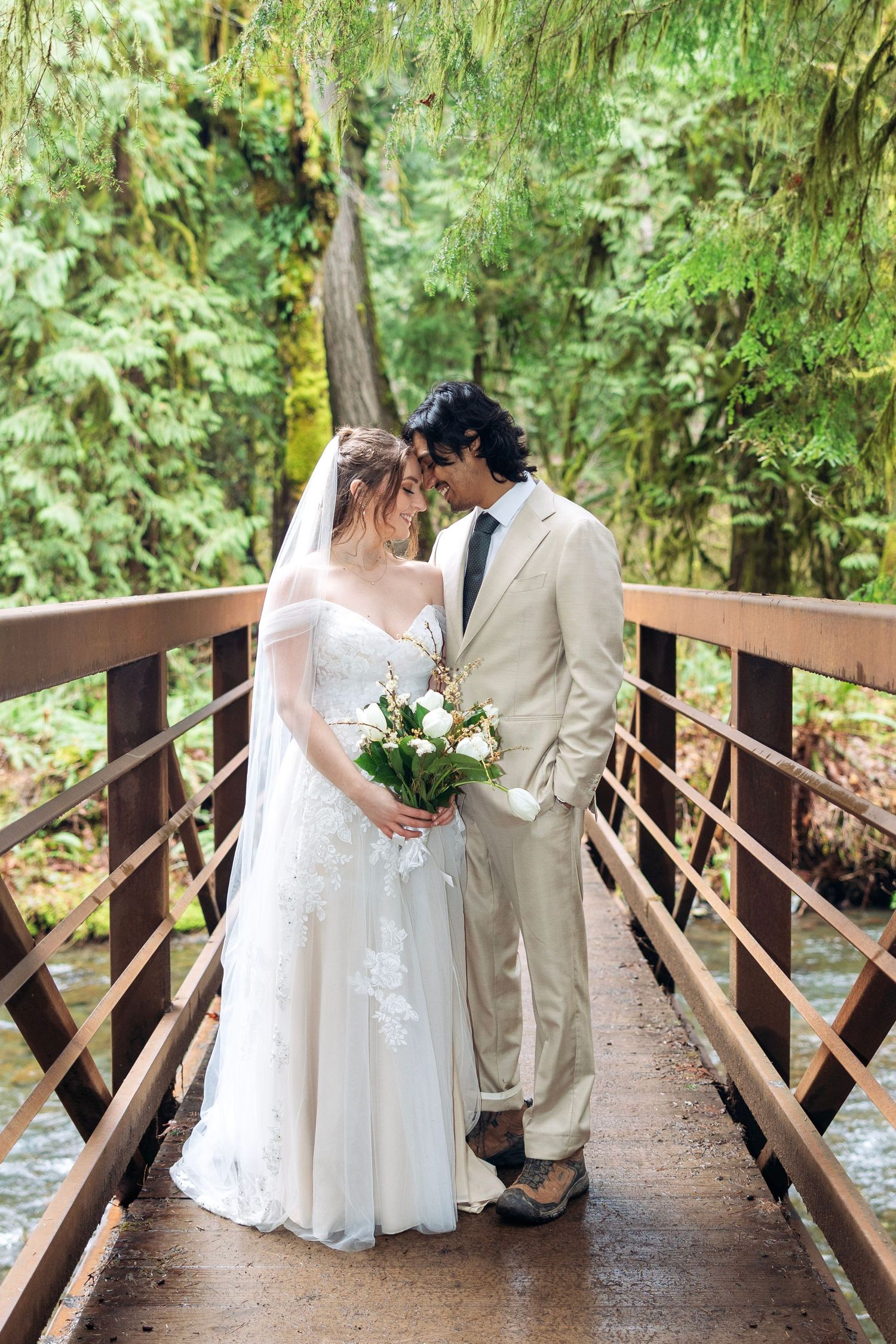 A romantic wedding couple shares intimate moments on a rustic wooden bridge surrounded by lush green forest.