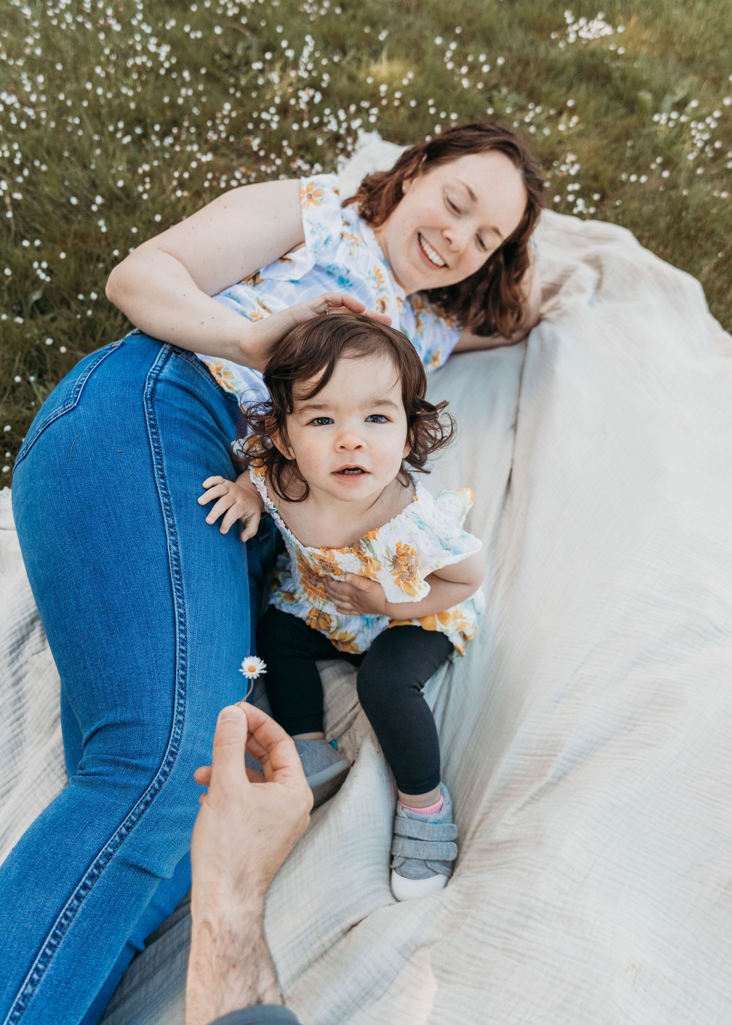 Mother and baby lying on white blanket outdoors sharing sweet moments together in casual denim attire.