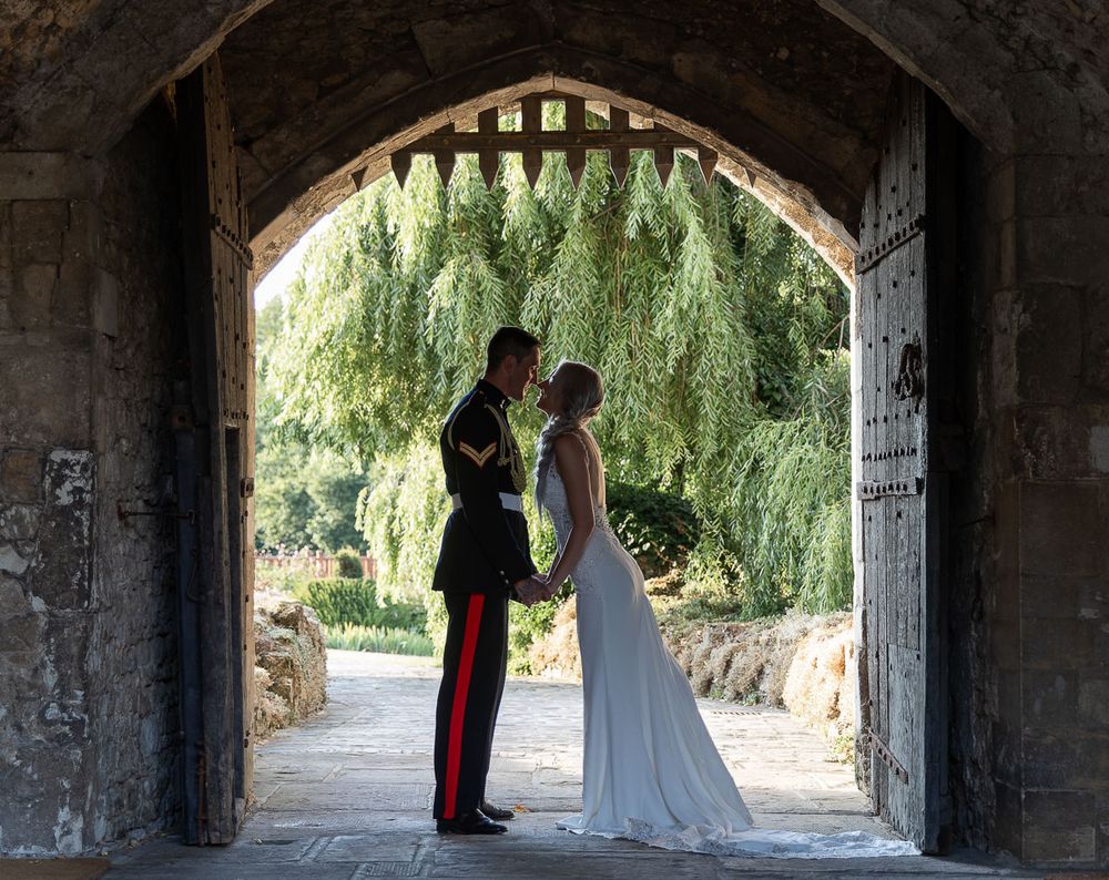 A romantic wedding couple silhouetted against the drawbridge of Allington Castle, with willow trees visible in background.