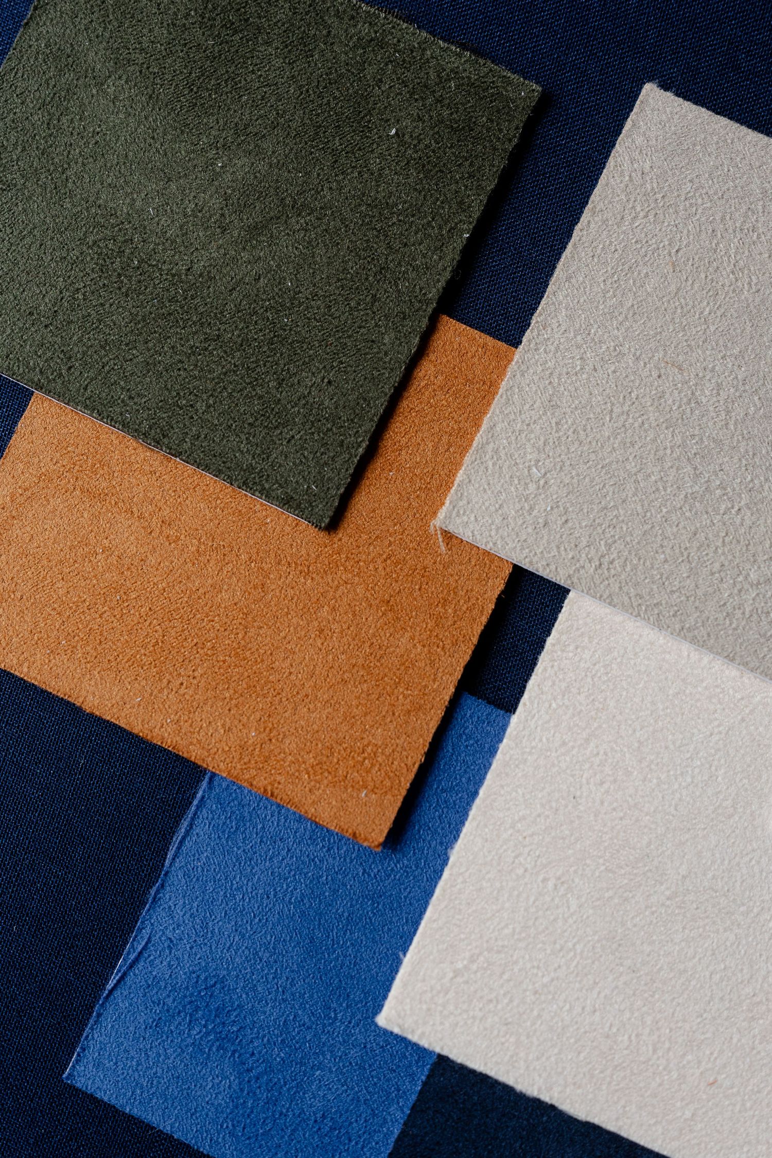 Overlapping fabric or leather swatches in green, tan, white, and blue colors arranged on a dark blue background.
