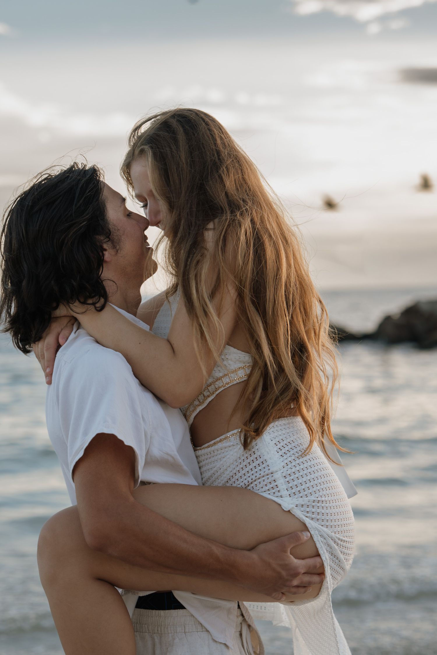 A romantic couple embraces in ocean waves during sunset creating an intimate beach photoshoot moment.