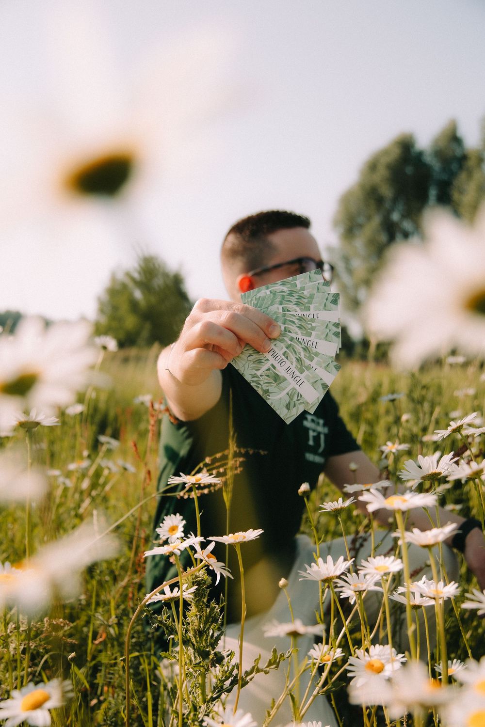 Een man die een stapeltje visitekaartjes vasthoudt in een zonnig madeliefjesveld | Brandingshoot