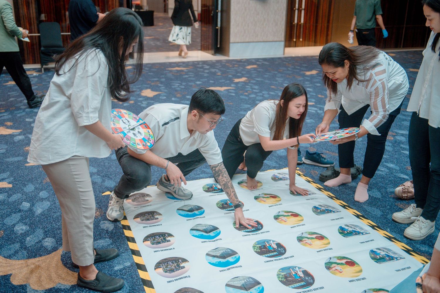 People playing Twister game on a white mat with colorful circles during an indoor party.