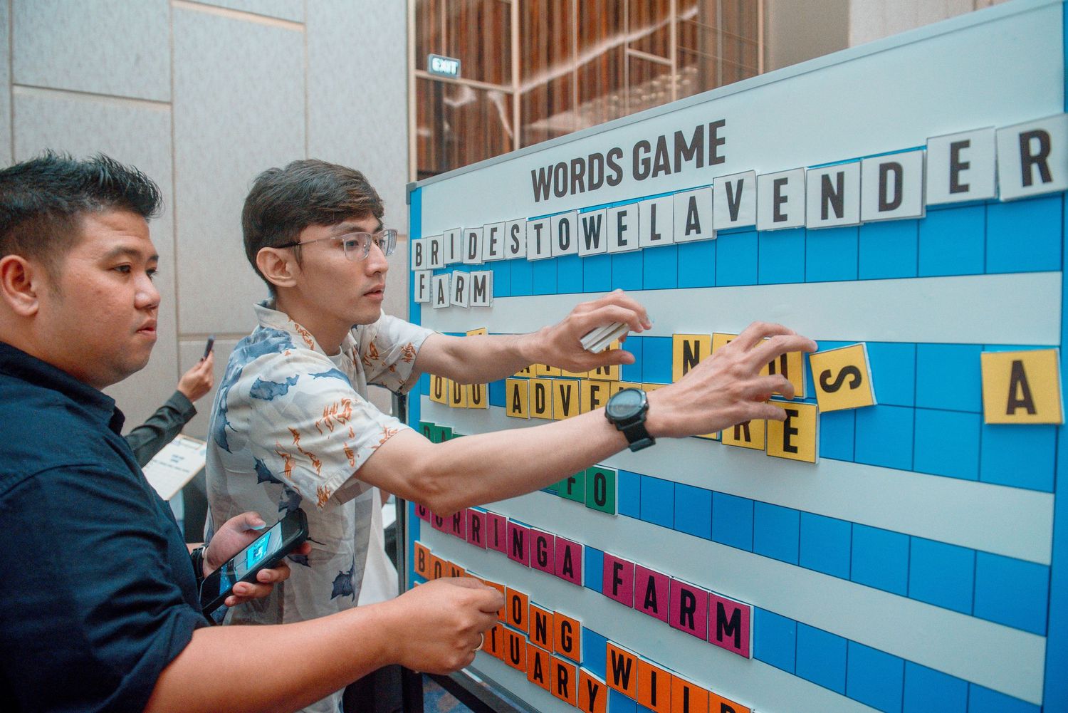 Students engage with a colorful word game display mounted on a bright blue wall in an educational setting.