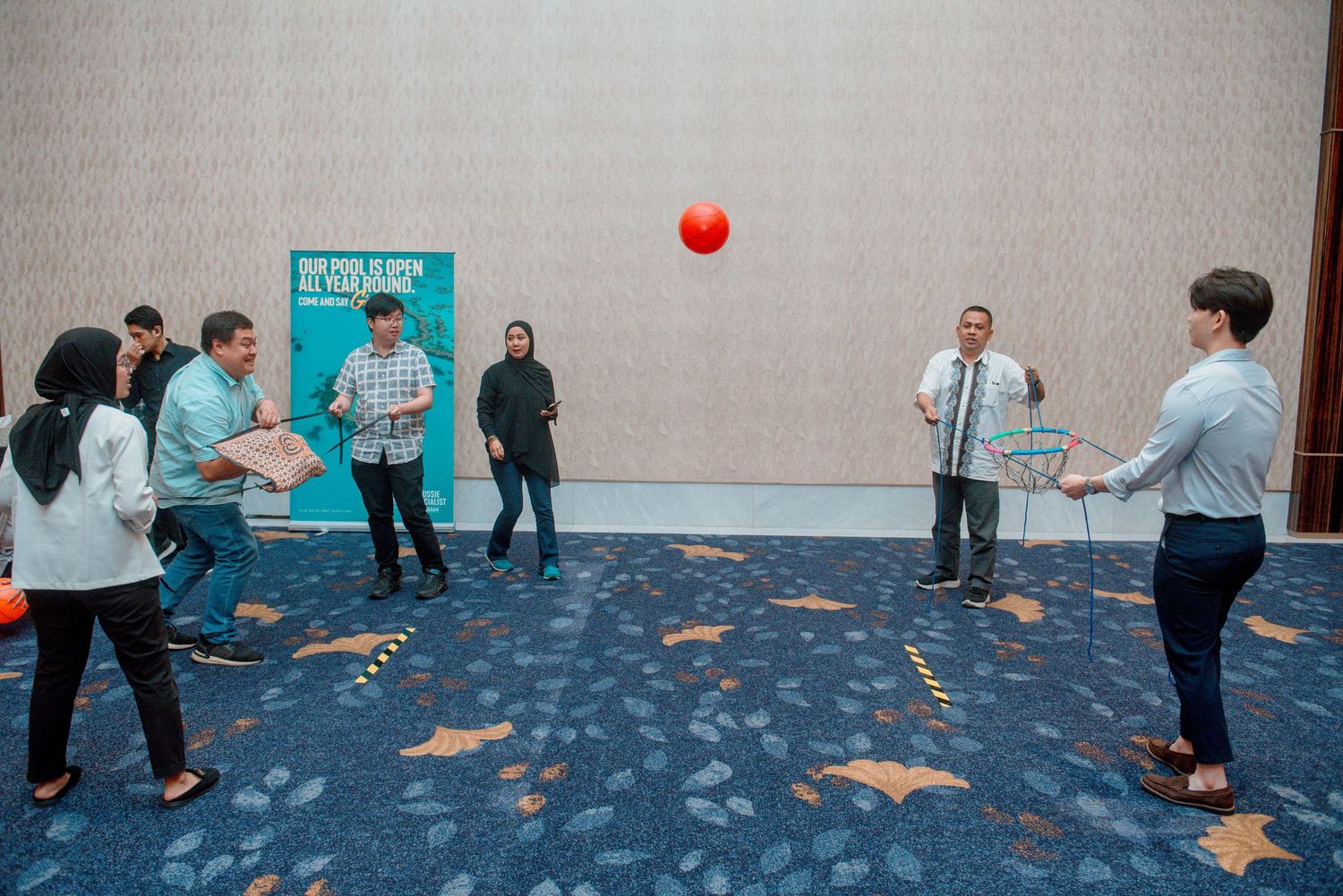 A group of people playing a team building exercise with red balls in a large indoor space.