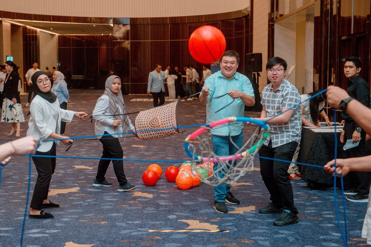 People playing a game with red balloons in a large indoor space with tiled flooring.