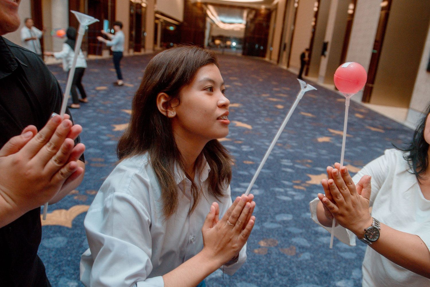 A person wearing a white shirt and jeans claps their hands while standing in a hallway.