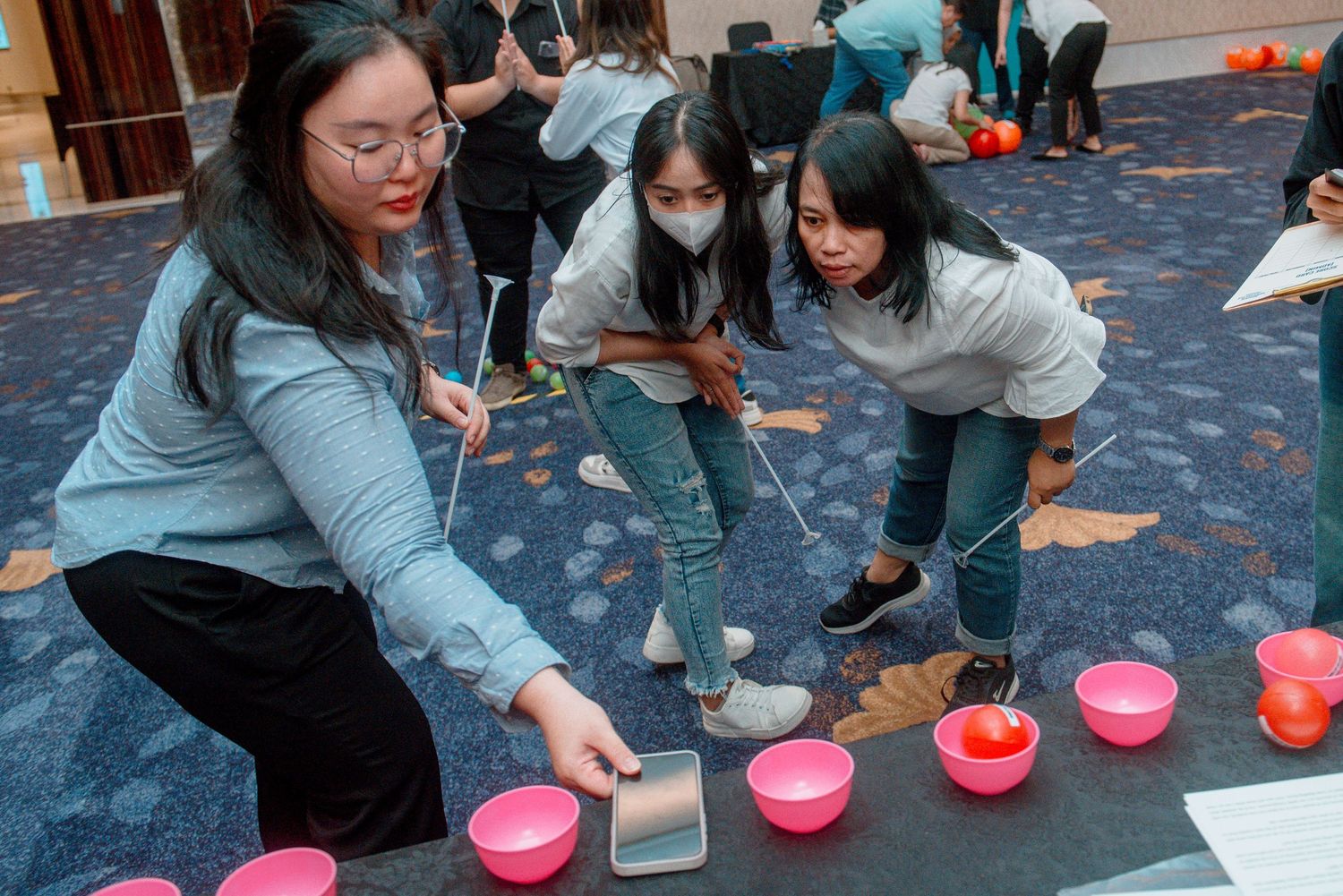 Students participate in a hands-on learning activity with pink bowls and scientific equipment on a blue carpeted floor.