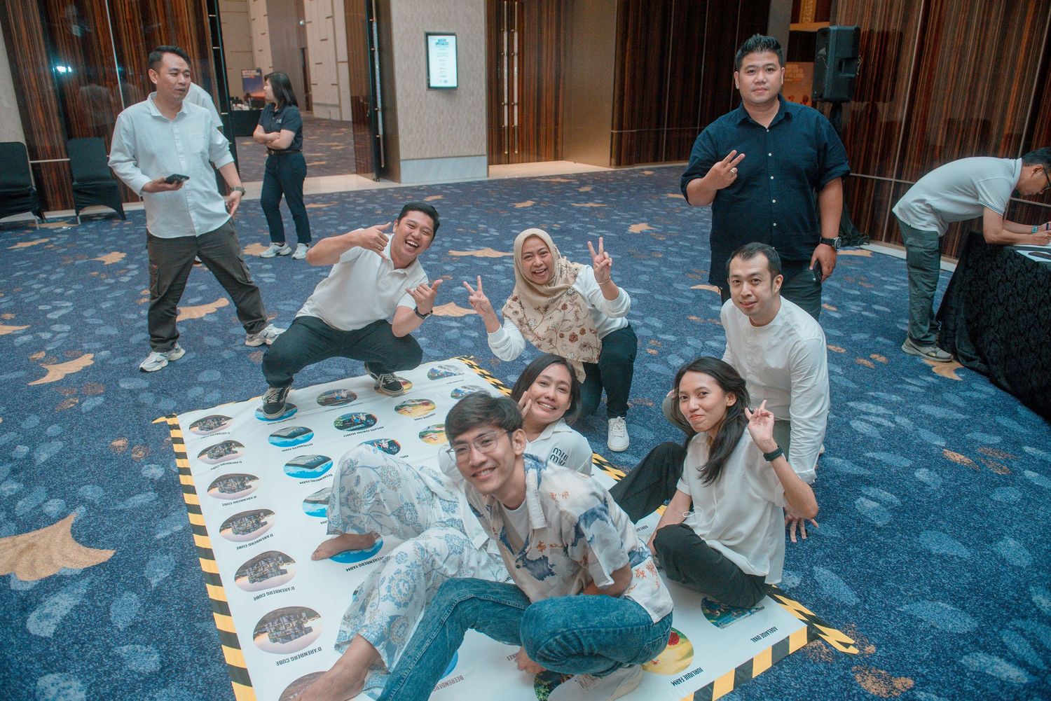 Group of people sitting on blue carpeted floor eating meals together at a casual gathering.