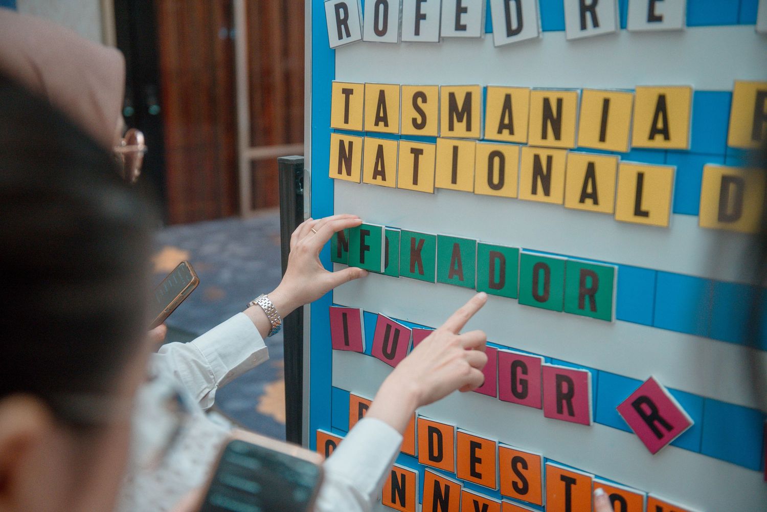 Close-up view of letter tiles on a blue Scrabble board showing parts of words being formed during gameplay.