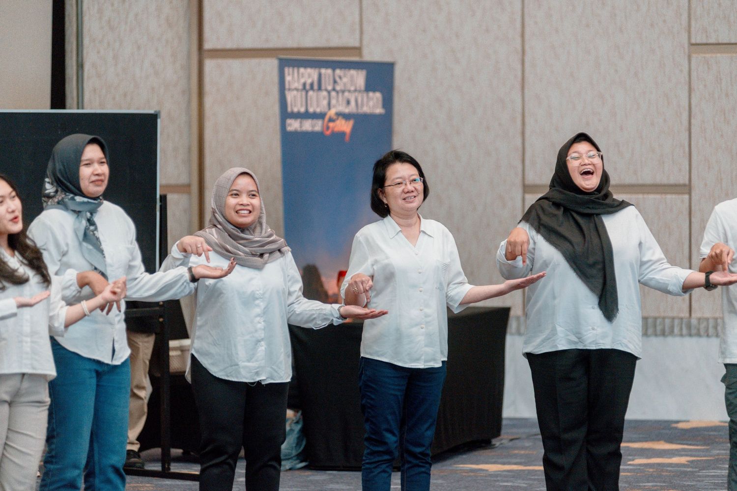 Group of people in white shirts stand in a line with their arms outstretched in a team building exercise.
