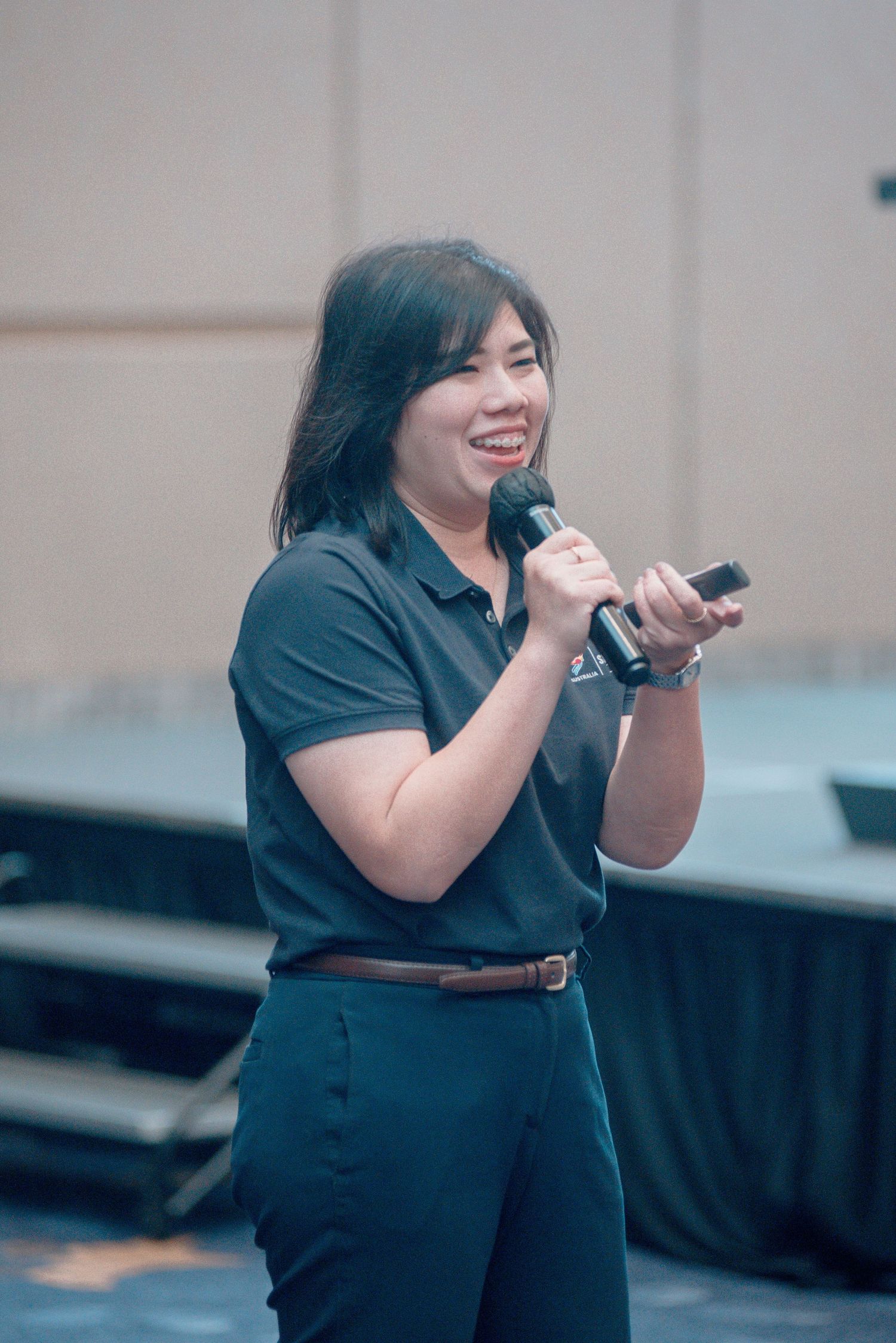 A performer in black attire sings passionately on stage during a live performance.