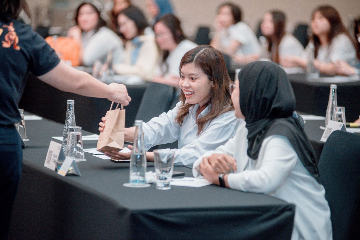 Medical professionals in white coats sit at tables during a conference or training session.