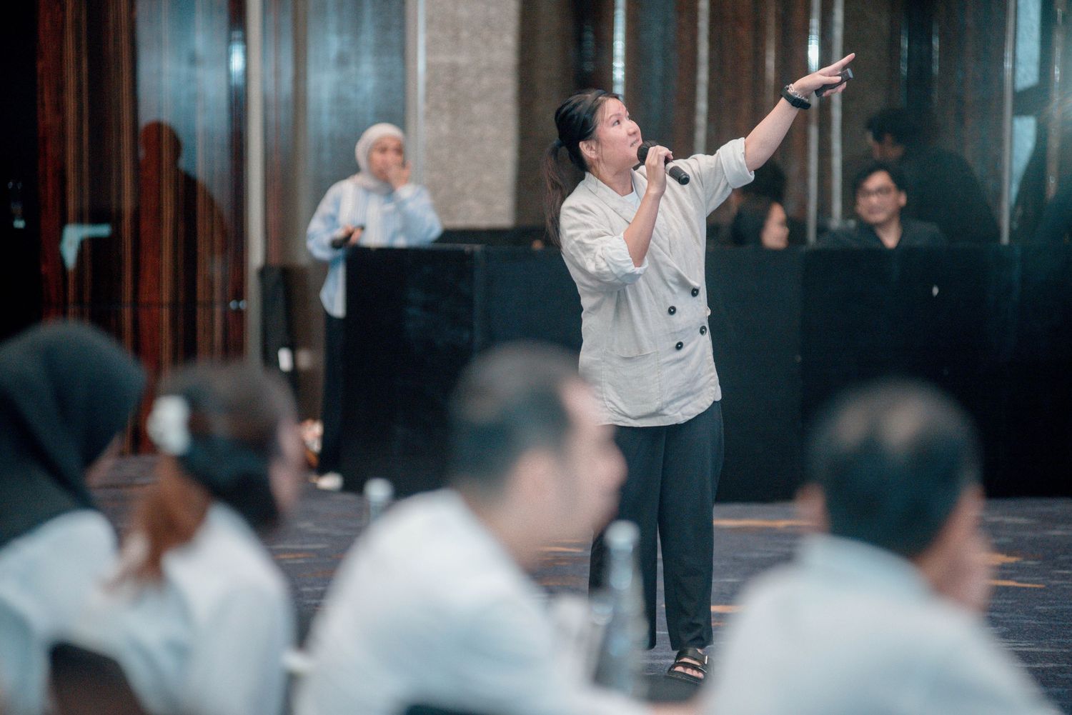 A person in white gestures dramatically while leading a group session in an indoor space.