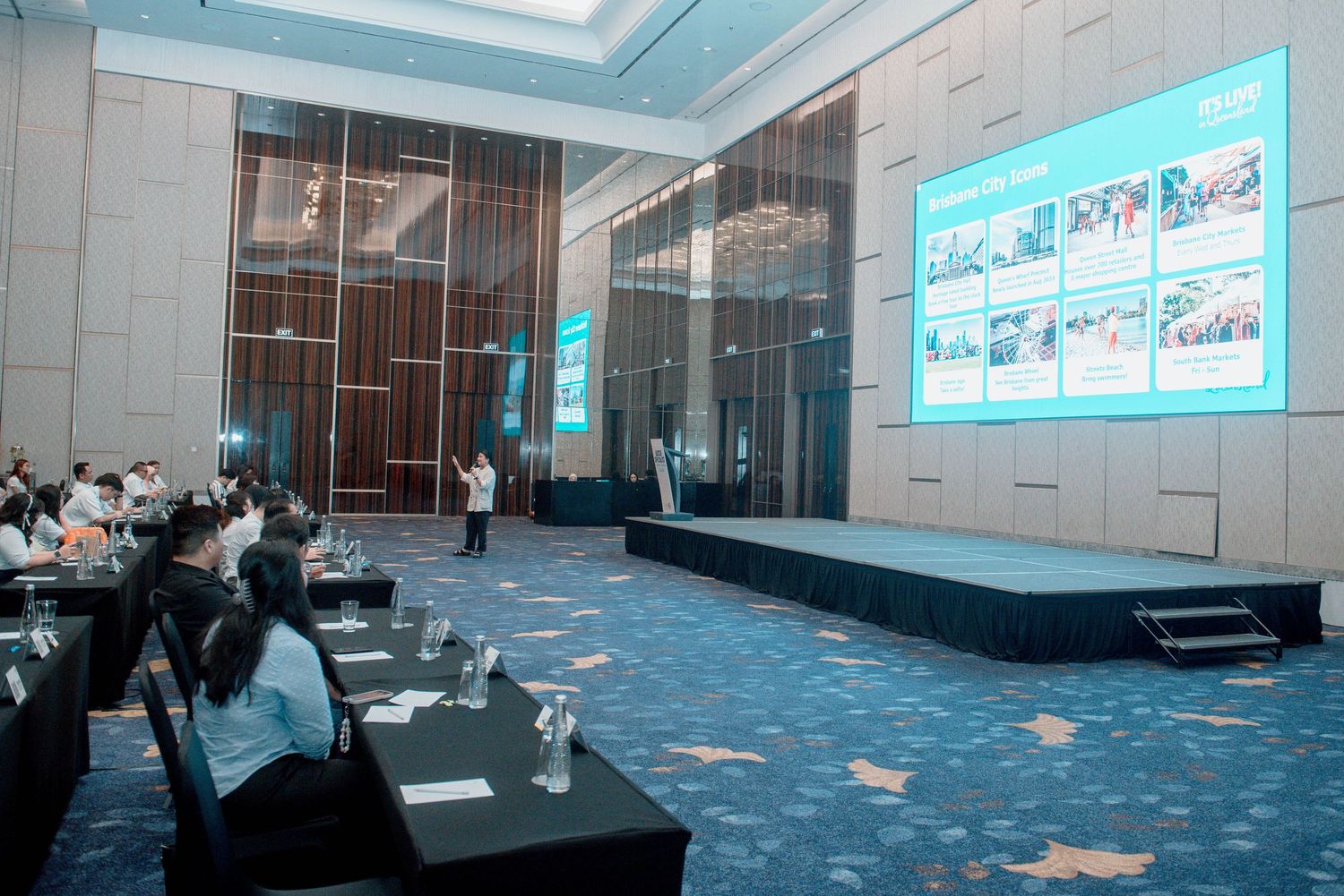 Conference room with blue carpeting, large projection screen, and audience seating arranged in rows for a presentation.