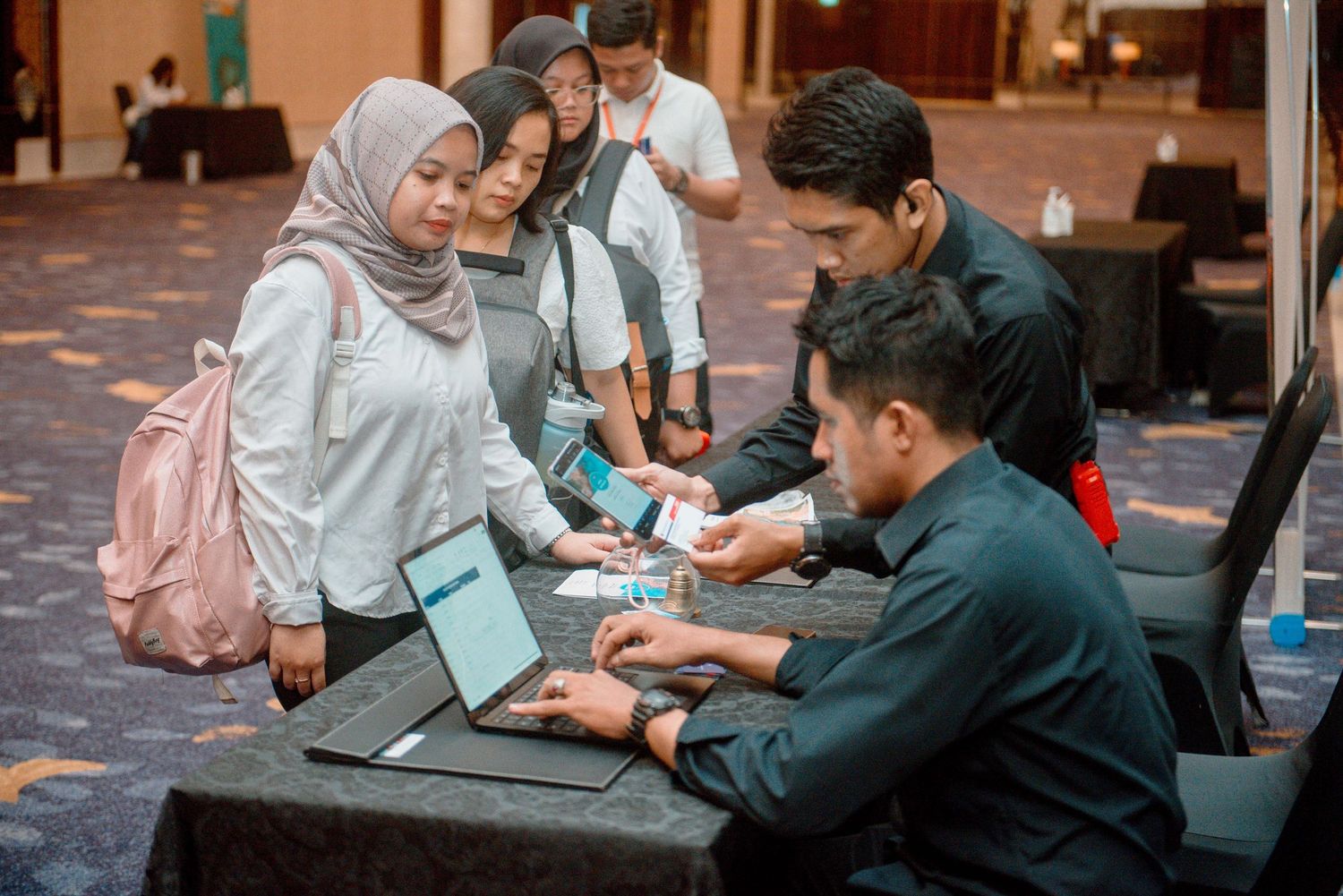 Students collaborate around a laptop computer during a study session in a carpeted hall.