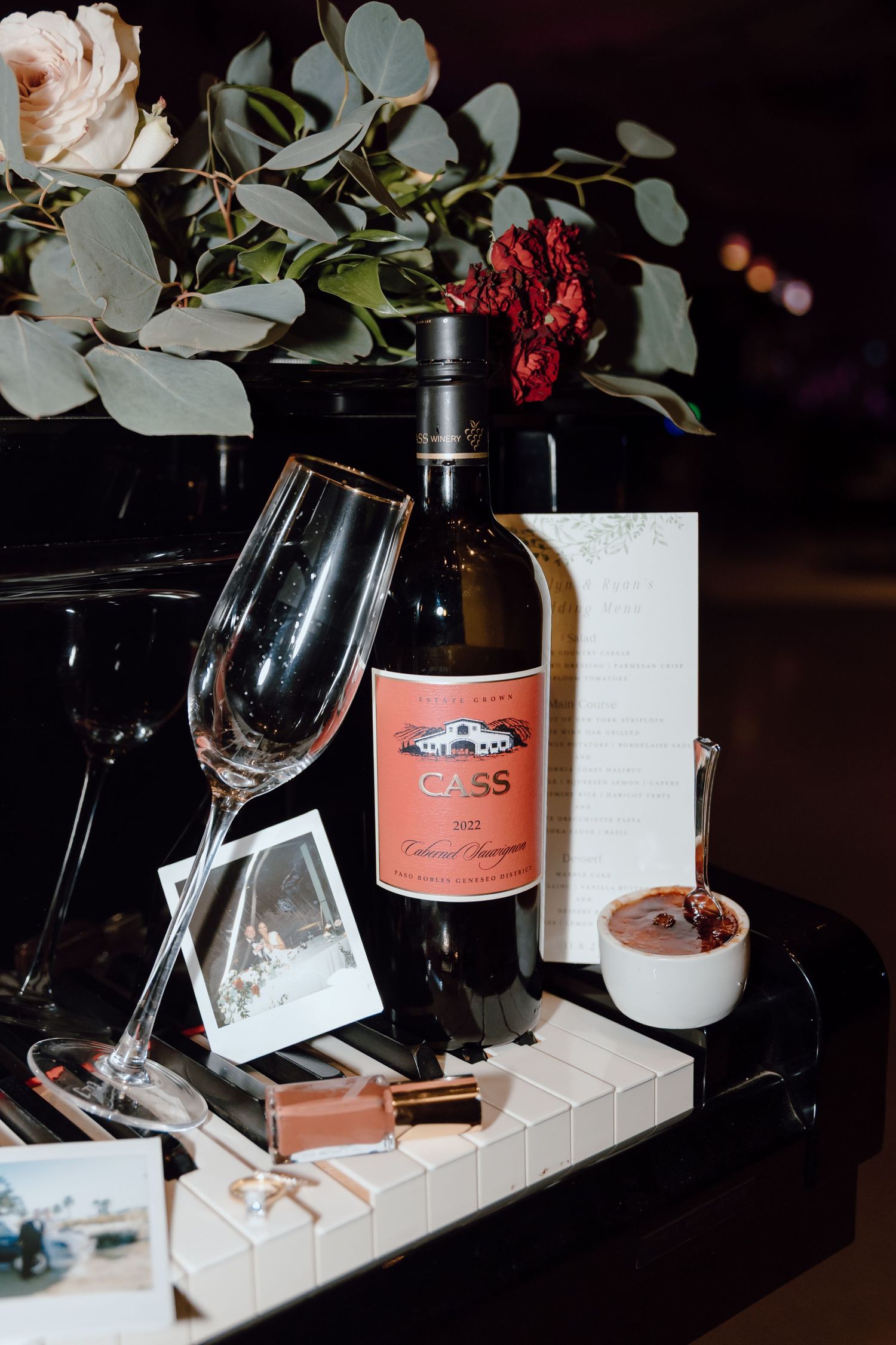 Elegant wine table setting with pink rose wine bottles, wine glasses, and eucalyptus leaves on white marble surface.