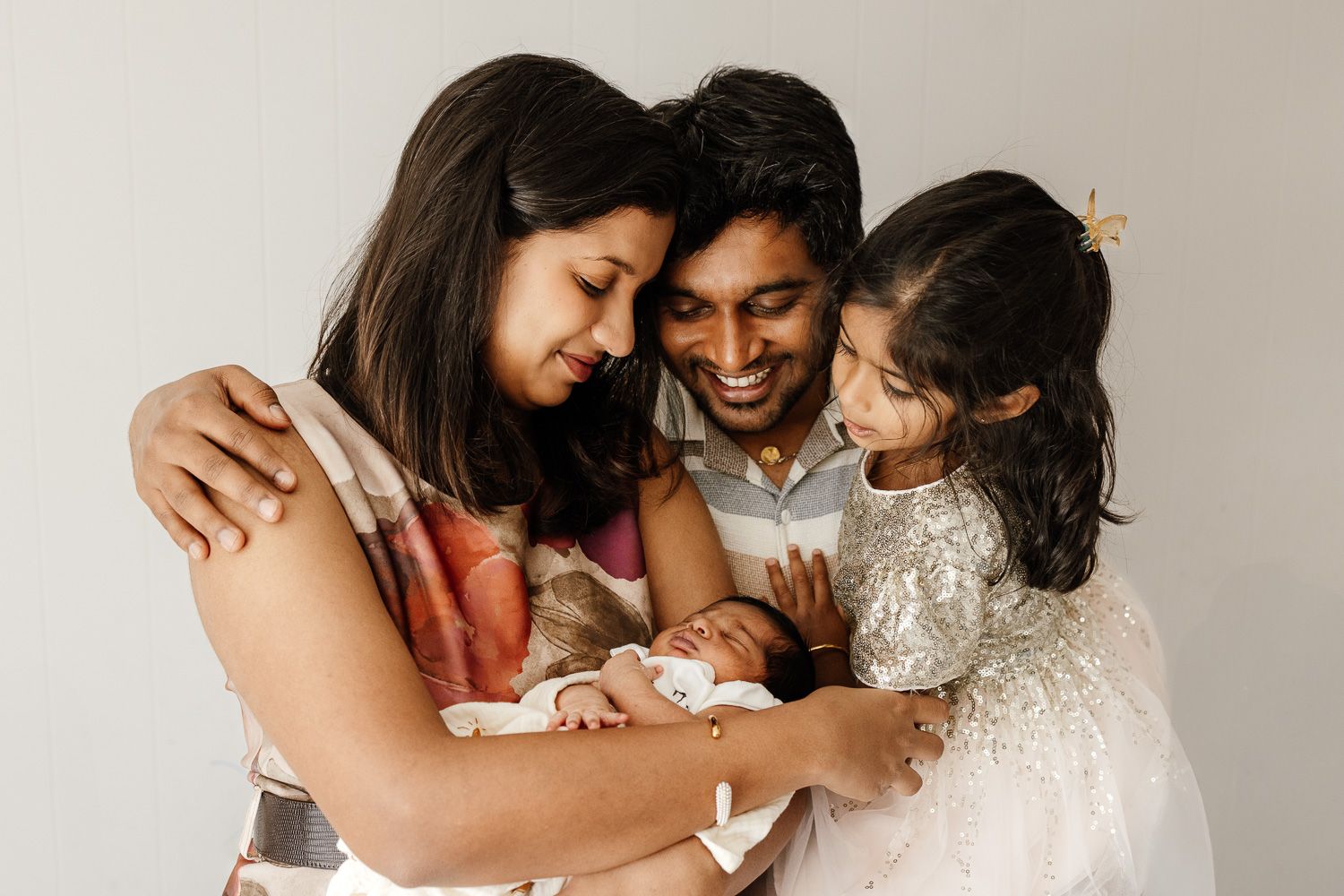San Jose family of four hug in front of a white wall during their in-home newborn photography session