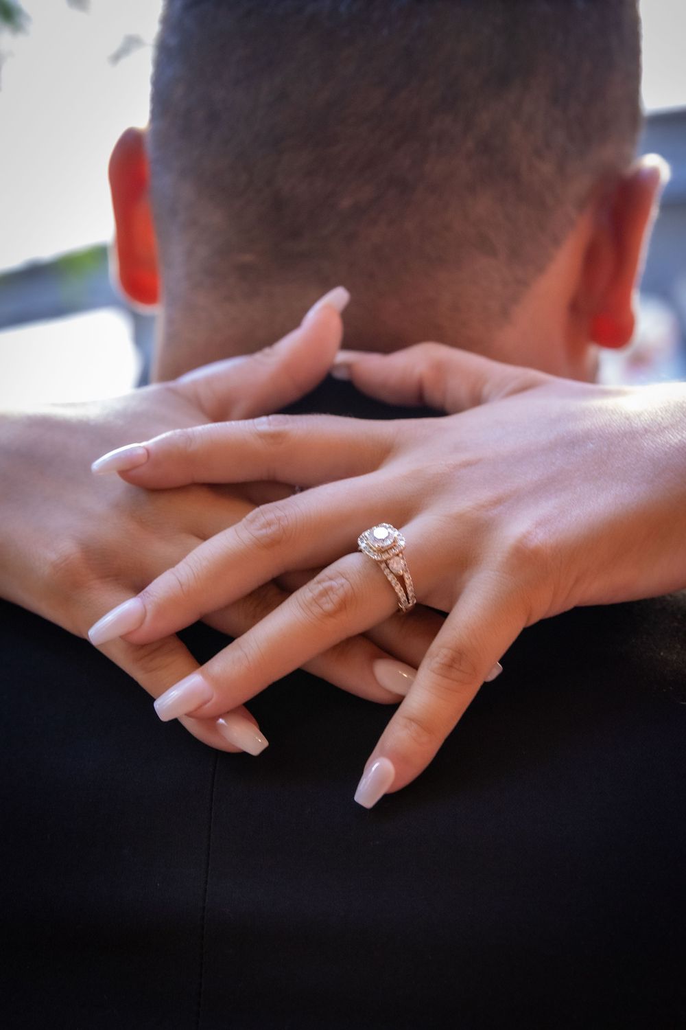 A close-up of hands embracing with an elegant diamond engagement ring displayed on manicured fingers.