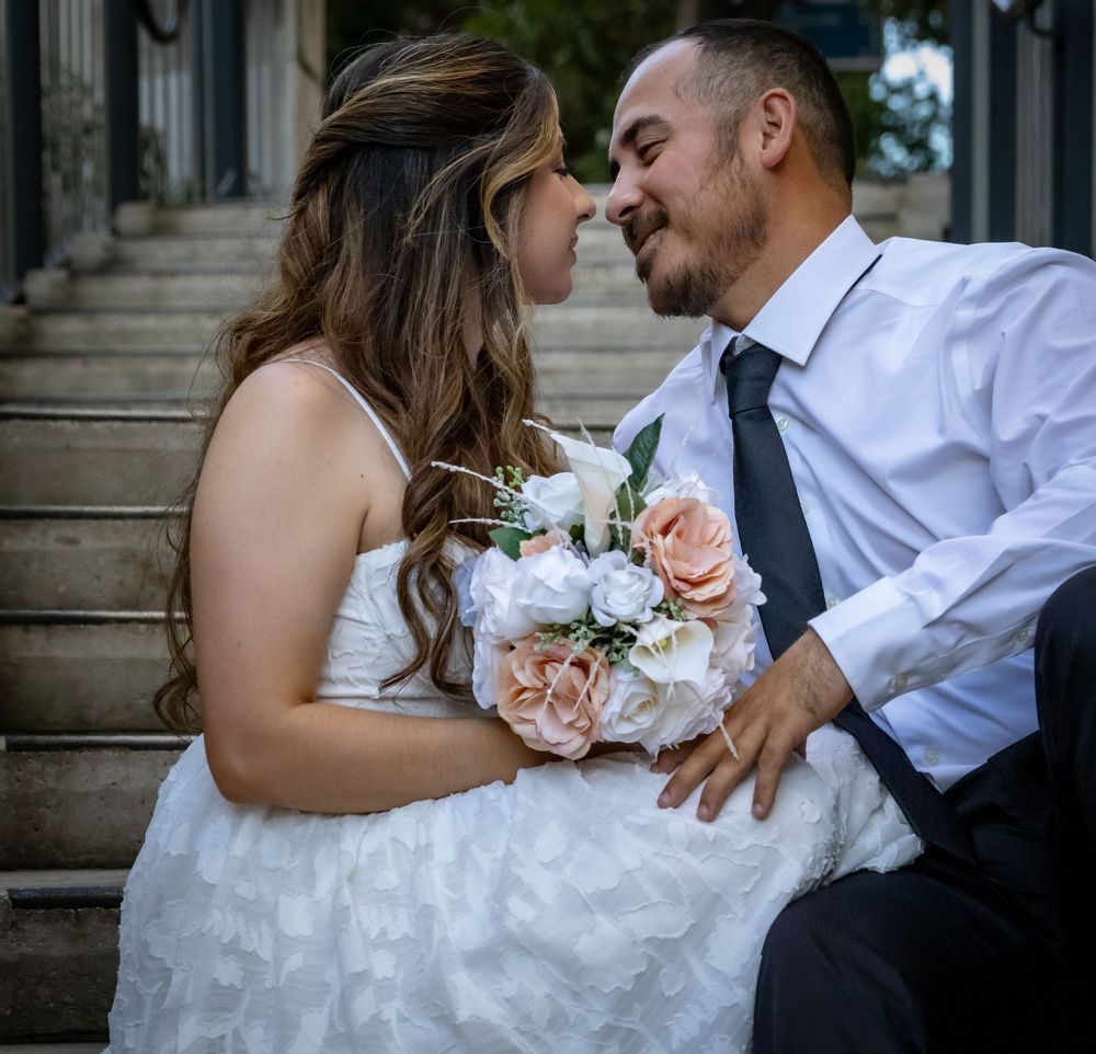A romantic wedding couple embraces on stone steps while holding a delicate pink and white floral bouquet.
