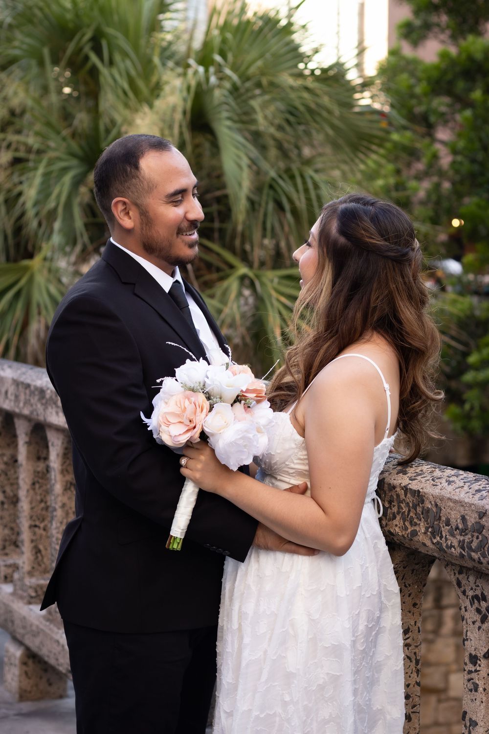 Newlyweds dance and laugh together in front of tropical palm trees during sunset.
