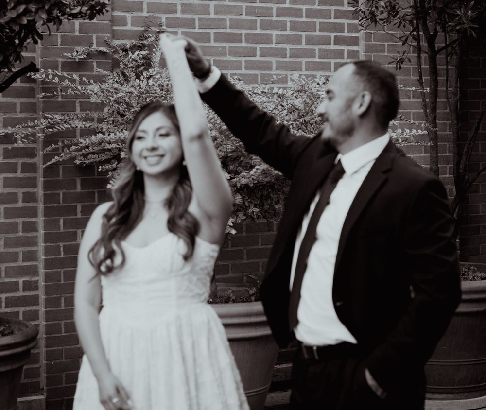 A series of four black and white wedding photos showing a couple dancing and twirling together against a brick wall.