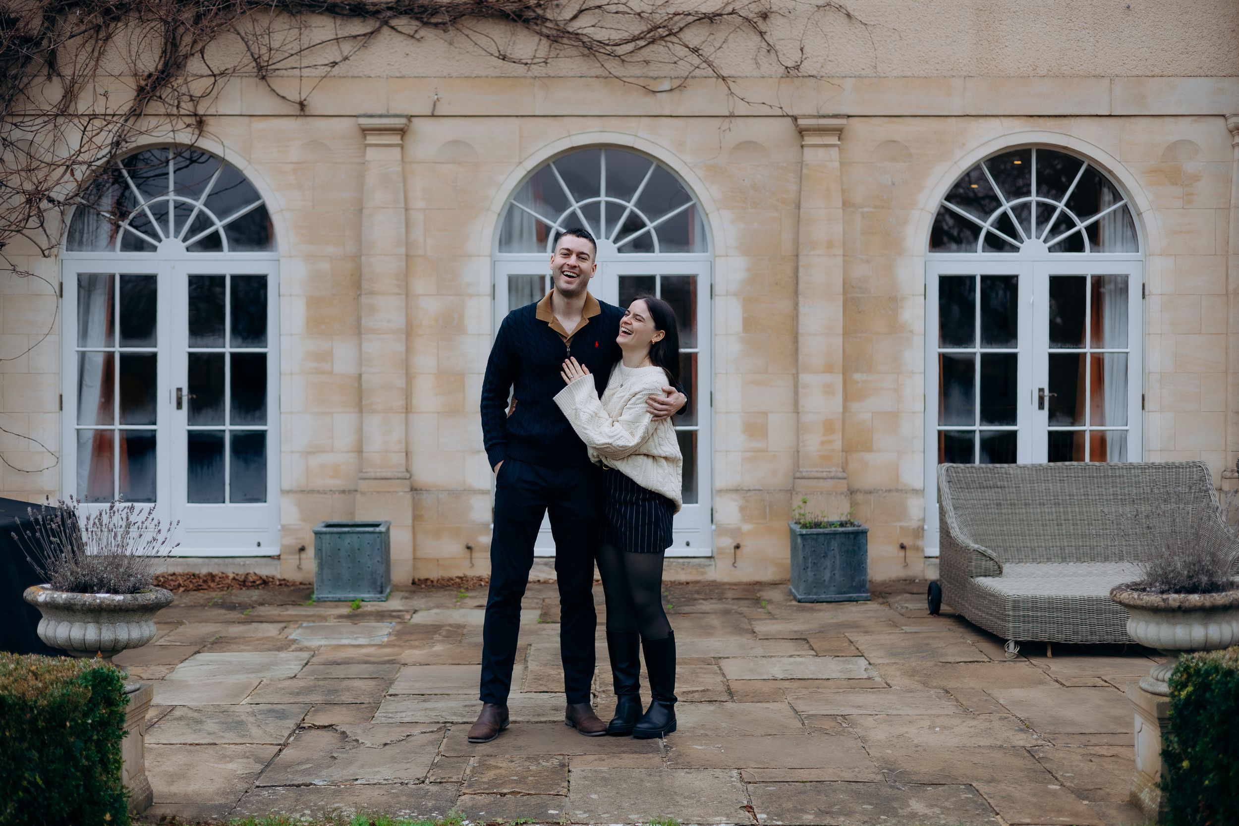 A couple shares a romantic moment in front of an elegant stone building with arched windows.