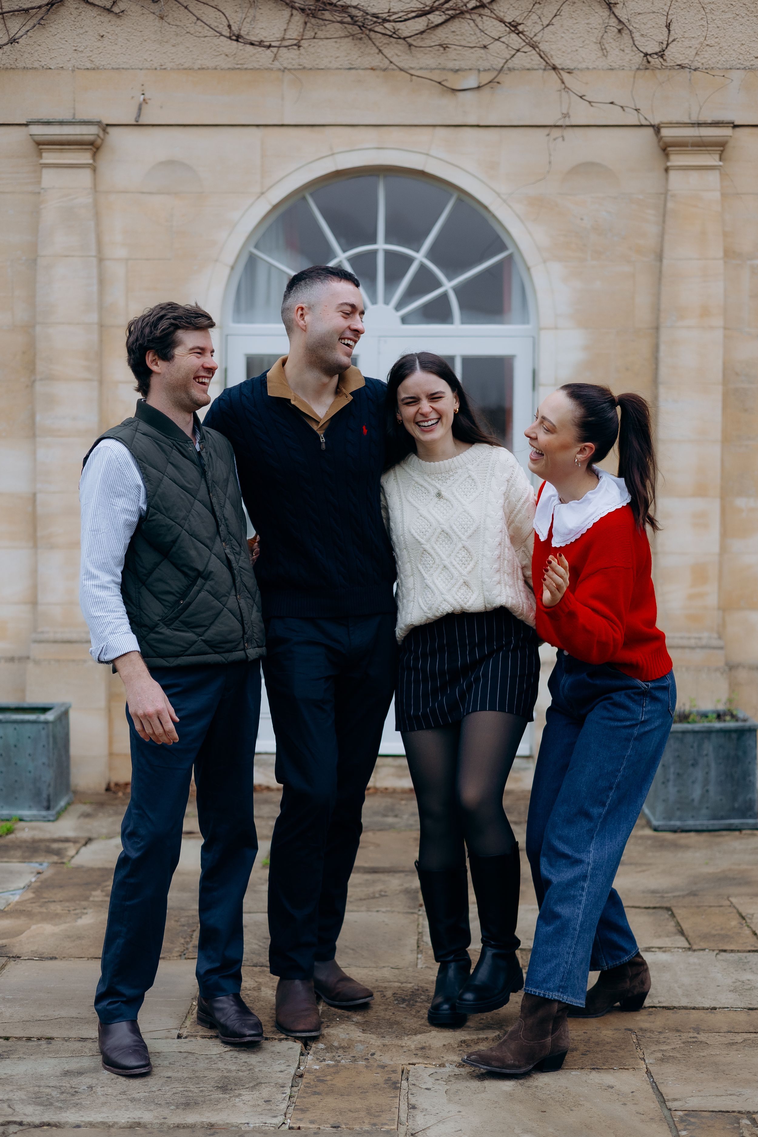 Group of people standing together and laughing against a stone building exterior.