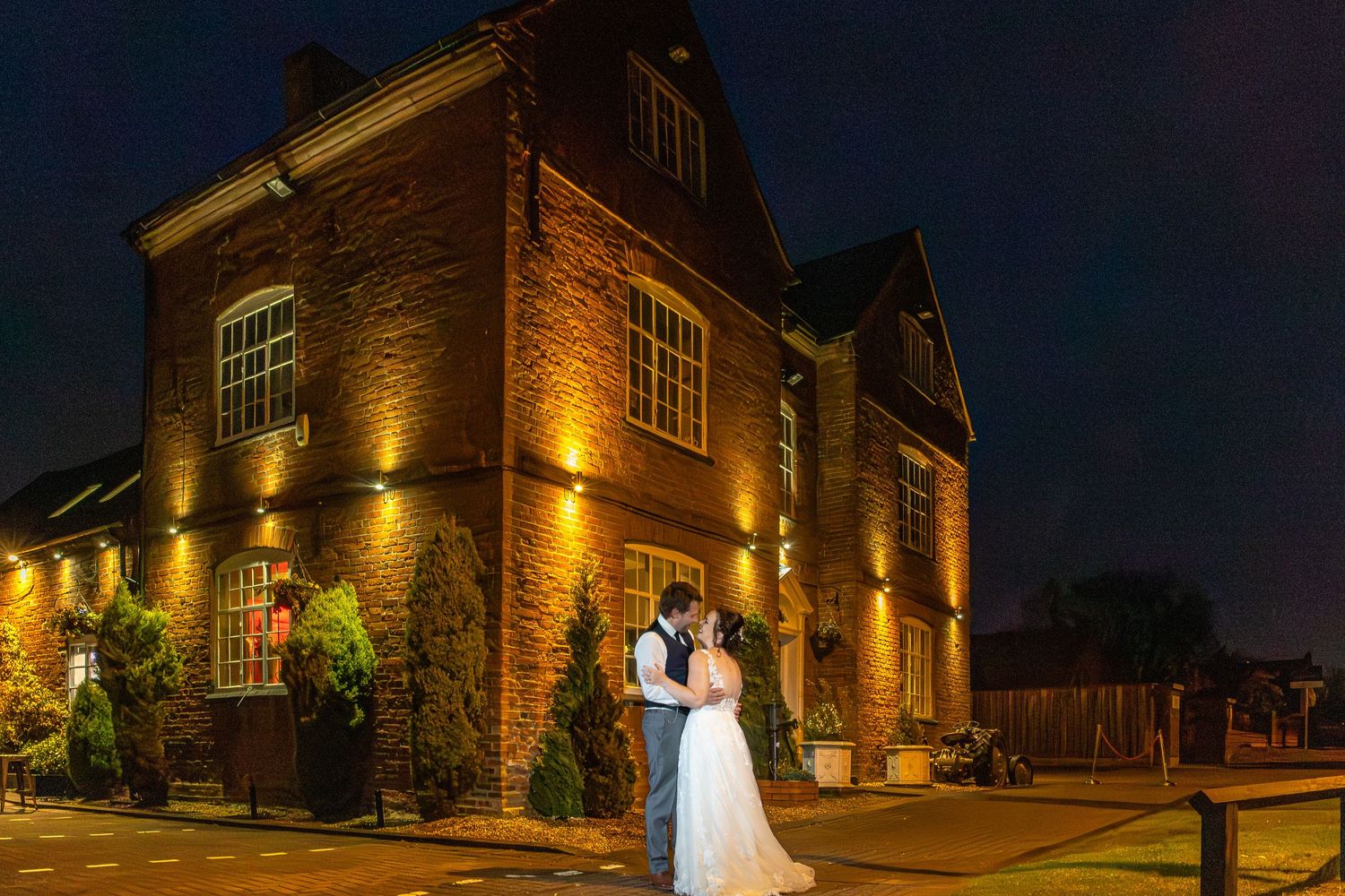 Elegant nighttime wedding photography at a historic brick venue illuminated by warm amber lighting and architectural details.