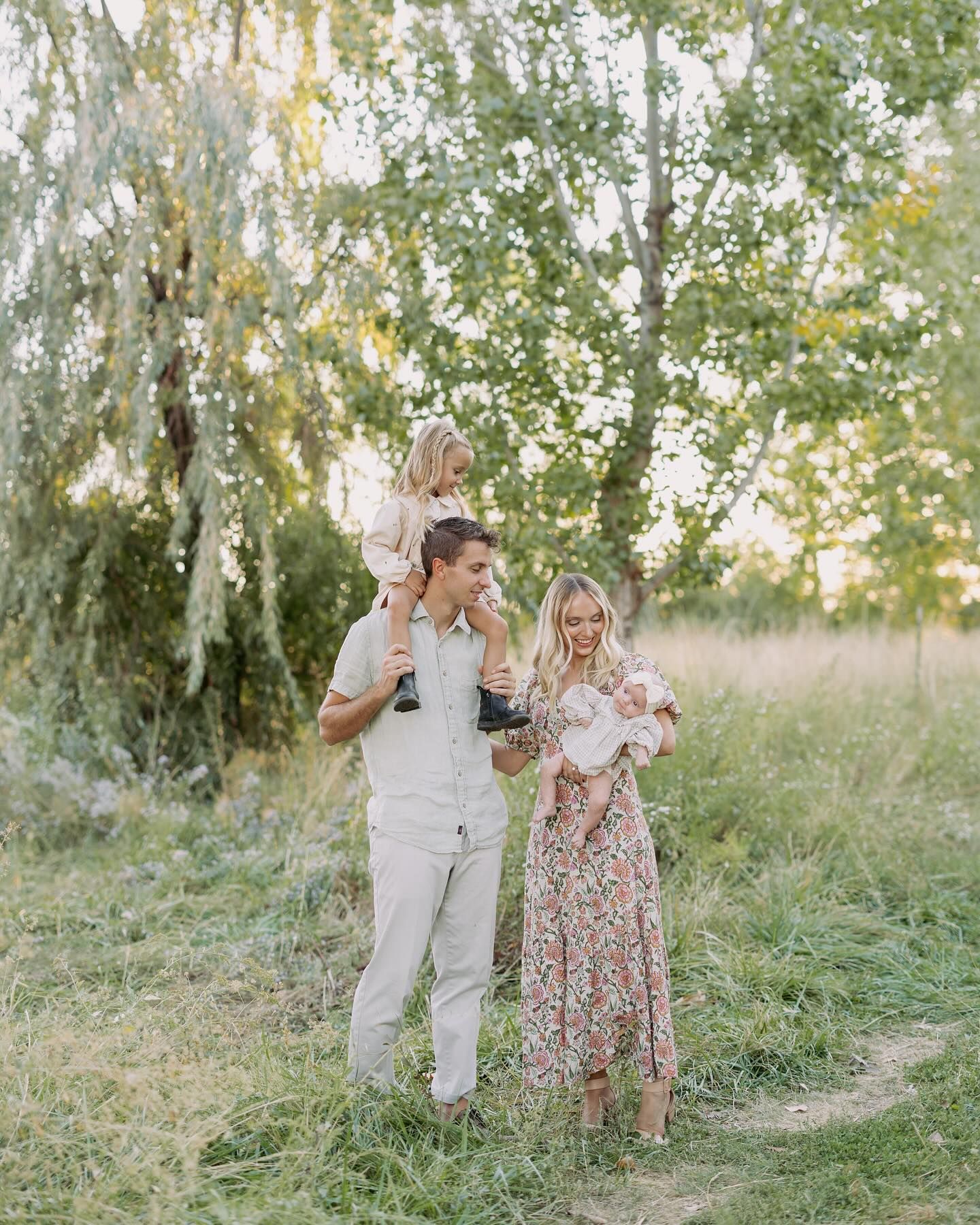 A couple walks together outdoors with their children in a dreamy natural setting with birch trees and tall grass.