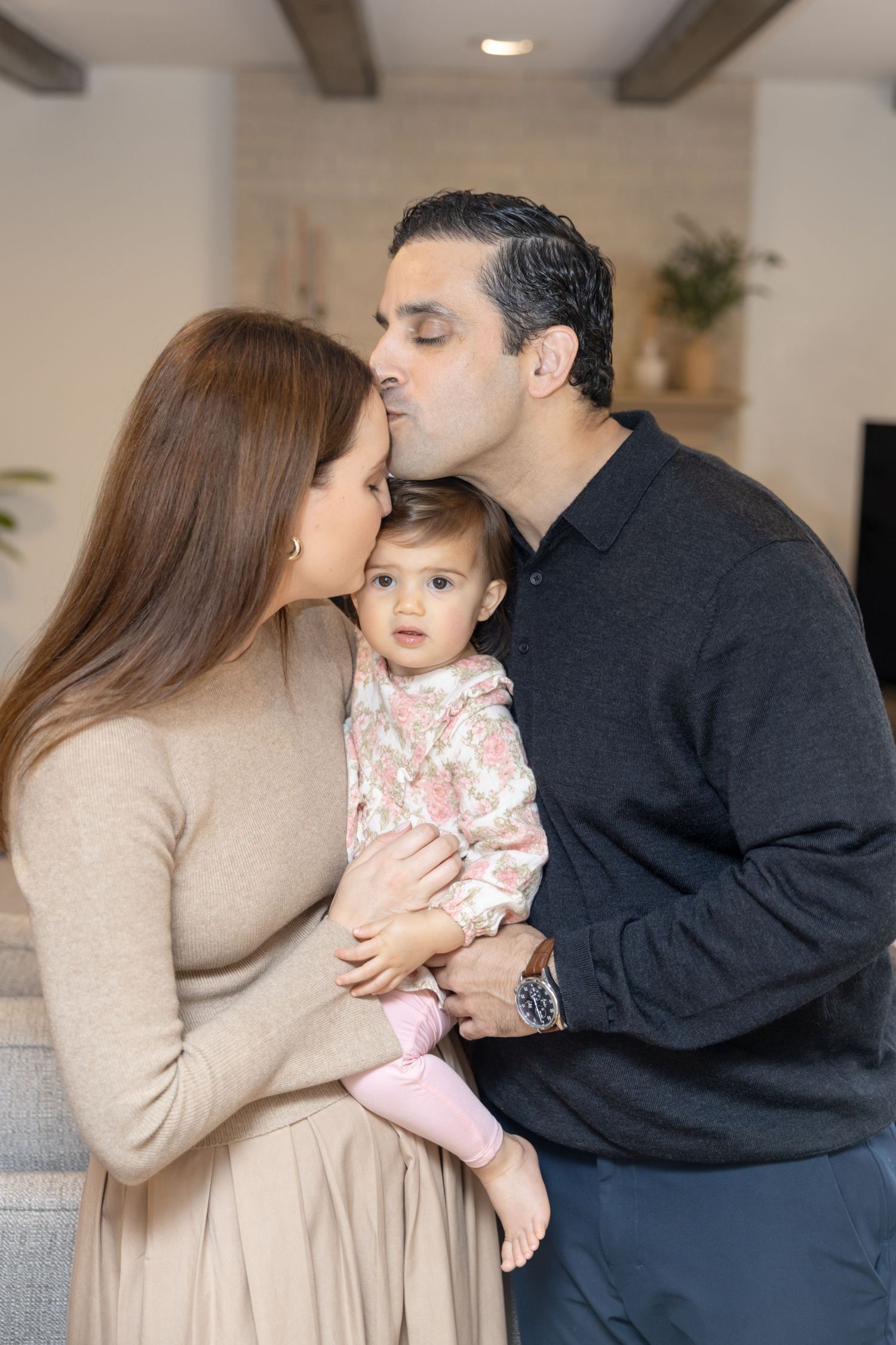 Parents share tender moments with their young child while sitting together on a gray couch at home.