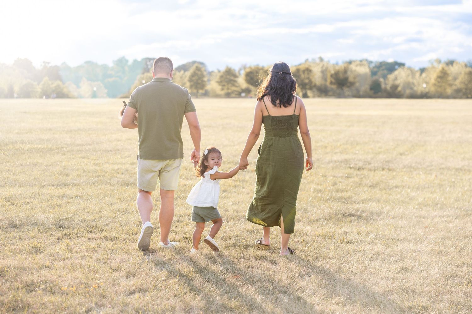 A family walking together through a golden field at sunset, viewed from behind as silhouettes.