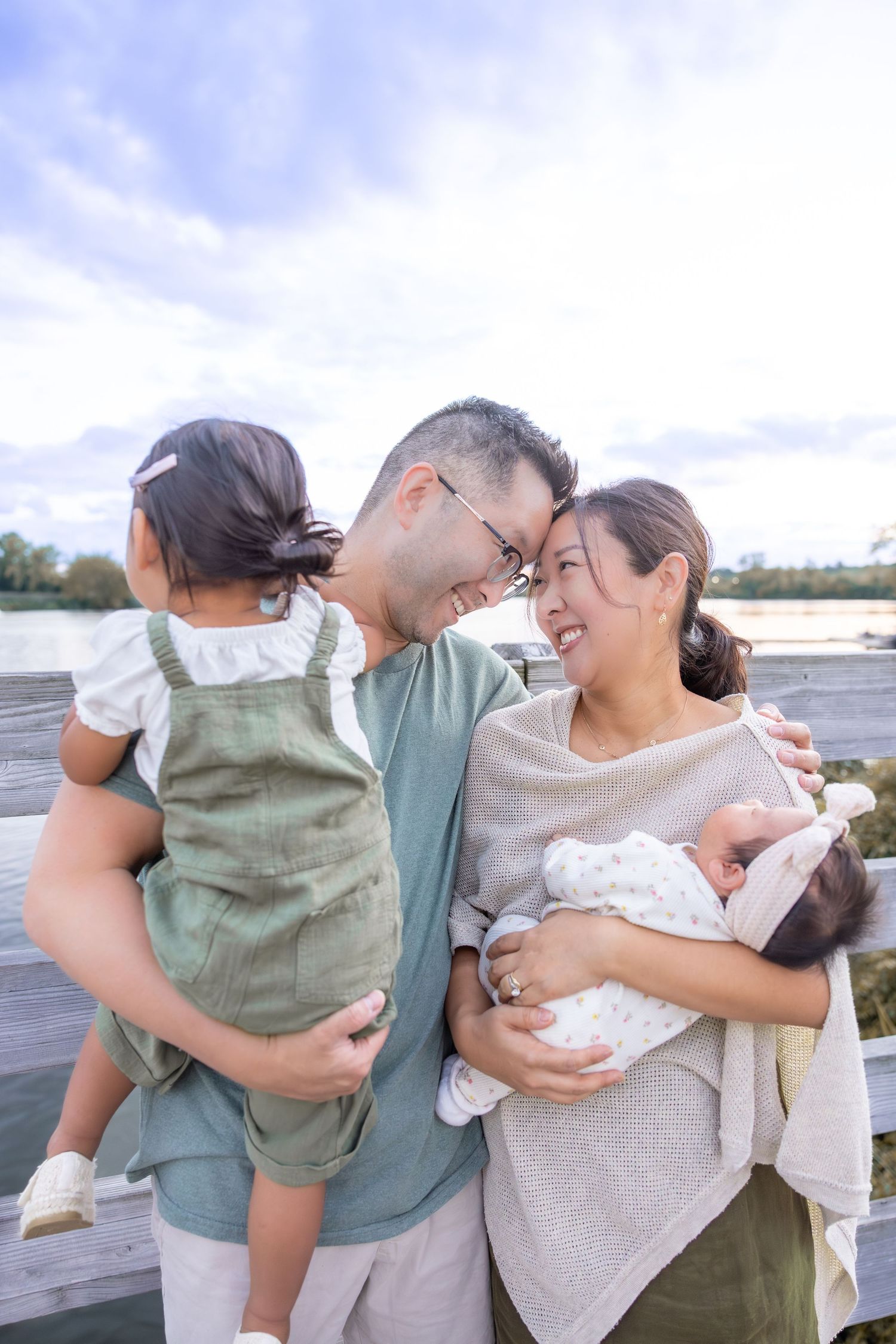 Family shares loving embraces and playful moments together on a waterfront dock during a sunny afternoon.
