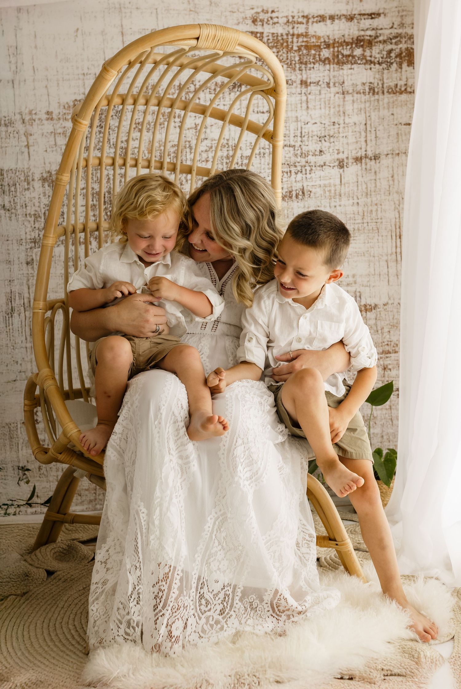 Mom in long lace dress cradles her sons on her lap during mommy and me session with Charlottesville family and baby photographer.