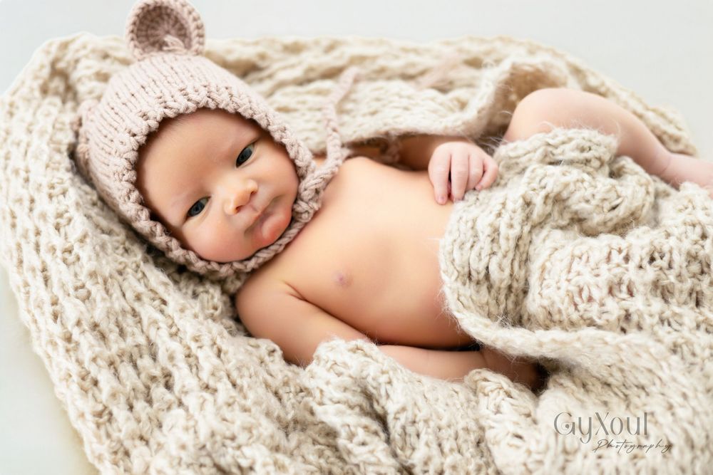 Newborn baby sleeping peacefully while wrapped in soft beige knitted blanket and wearing matching knit hat.