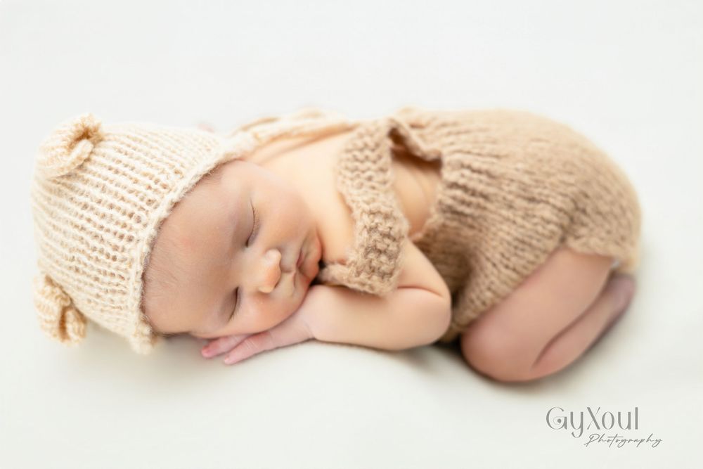 Peaceful sleeping newborn wearing soft knitted beige hat and wrap while curled up in fetal position.