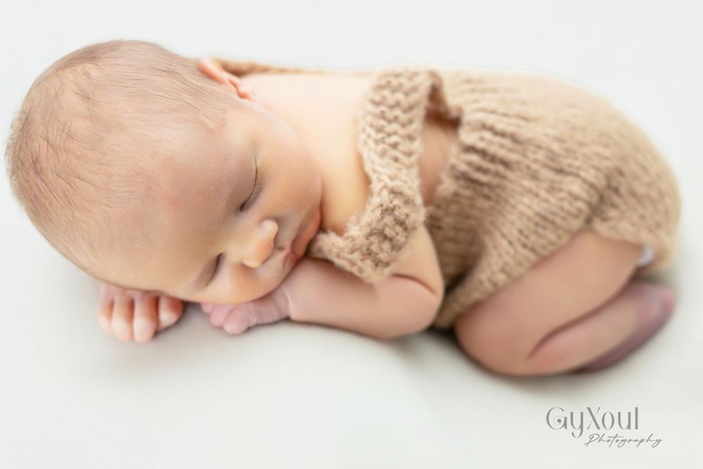 Newborn baby wrapped in soft beige knit blanket sleeping peacefully on white background.