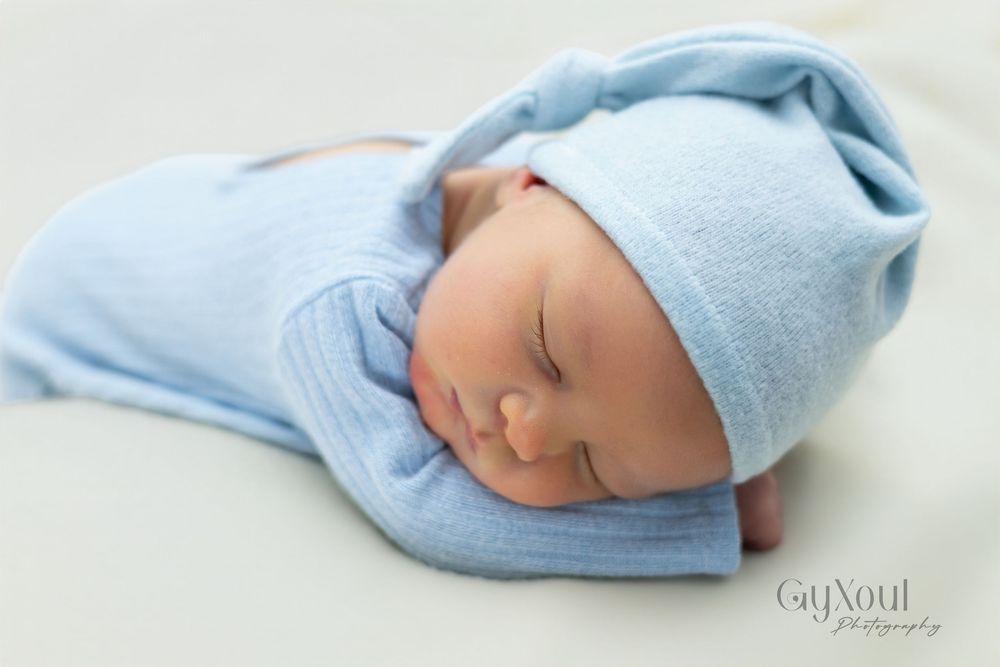 Five sequential photos show a sleeping newborn baby wrapped in a soft blue blanket on white bedding.