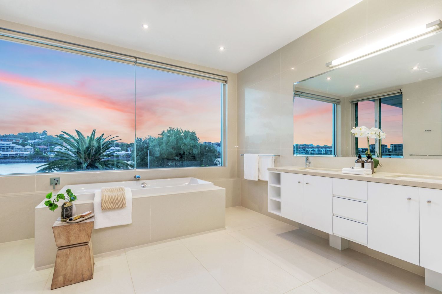 Luxurious ensuite bathroom with freestanding bathtub, large window showcasing stunning pink and purple sunset views.