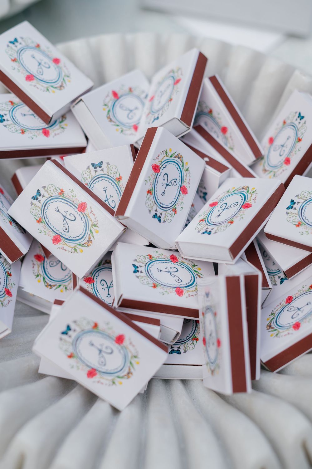 Decorative wedding matchboxes with whimsical blue and pink designs arranged on white fabric.