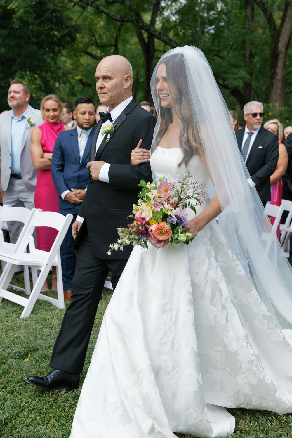 Outdoor wedding ceremony in a garden setting with white chairs and floral decorations.