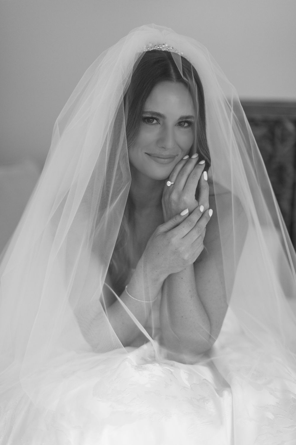 A bride wearing a traditional white veil poses for a classic black and white portrait.