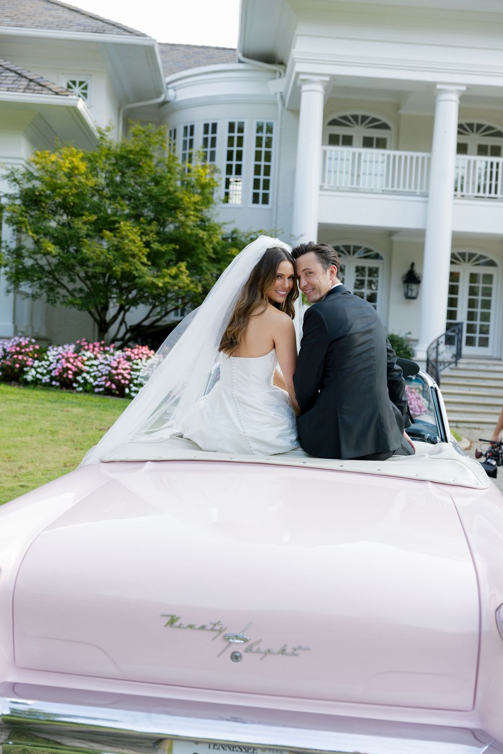 Romantic wedding photos taken with a classic pink vintage car at an elegant white mansion.