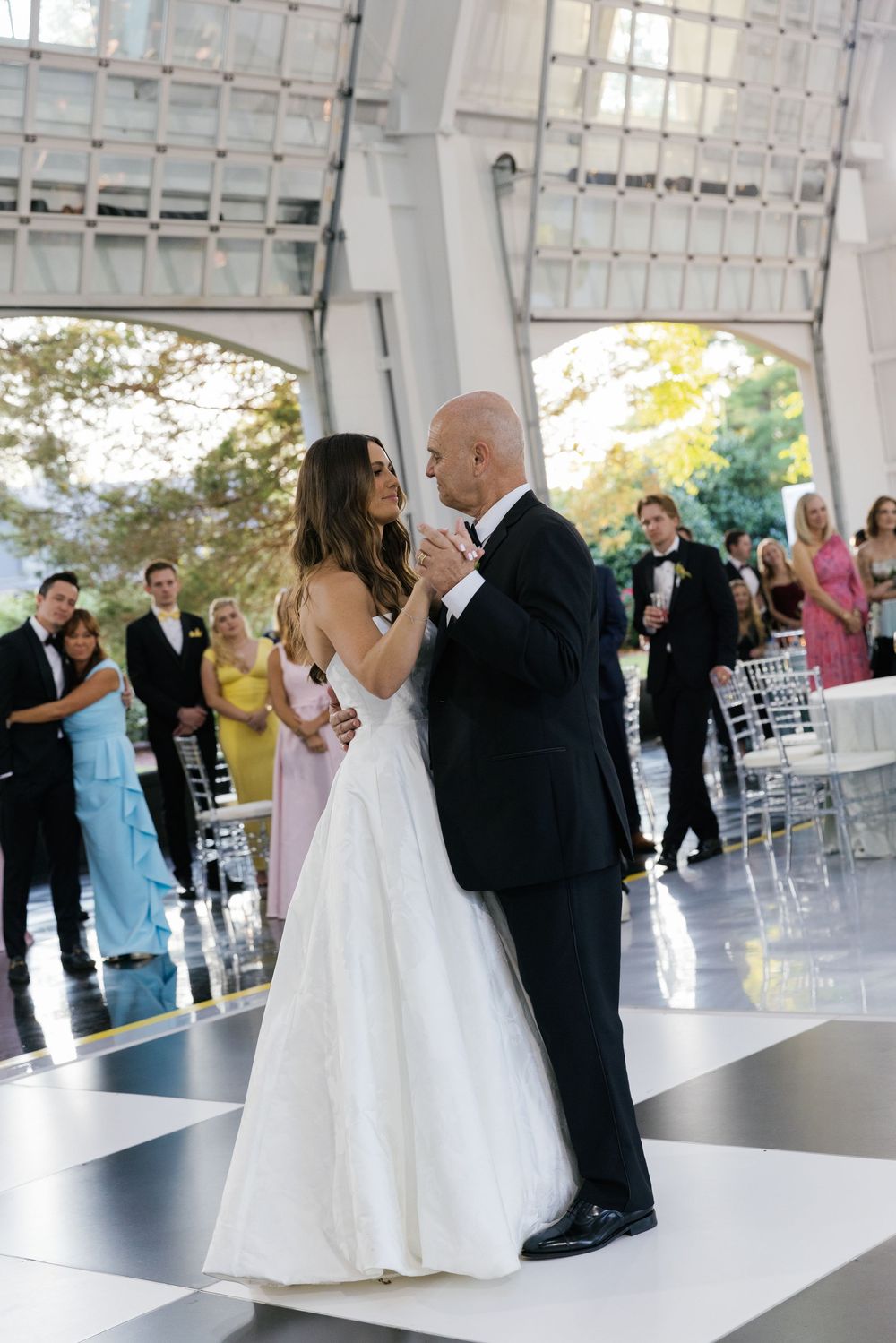 A couple shares their first dance as newlyweds on a black and white checkered dance floor at an elegant wedding reception.